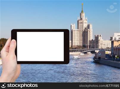 travel concept - hand holds tablet pc with cut out screen and Moscow vysotka - skyscraper on background