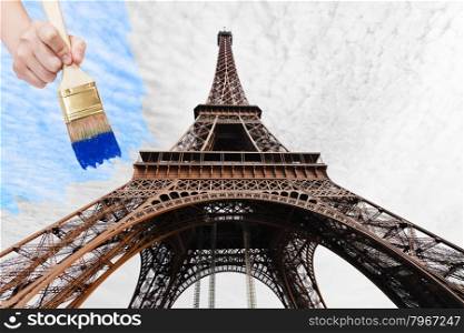 travel concept - hand with paintbrush paints blue sky over Eiffel tower in Paris city, France