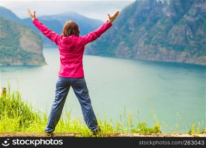 Travel concept. Happy free tourist woman in happiness and elated enjoyment with arms raised outstretched up looking at fjords mountains in Norway. Woman with raised hands in norwegian mountains fjords