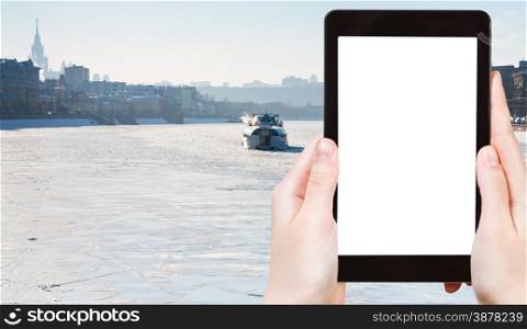 travel concept - tourist photograph iceboat on frozen Moscow river in sunny winter day on tablet pc with cut out screen with blank place for advertising logo