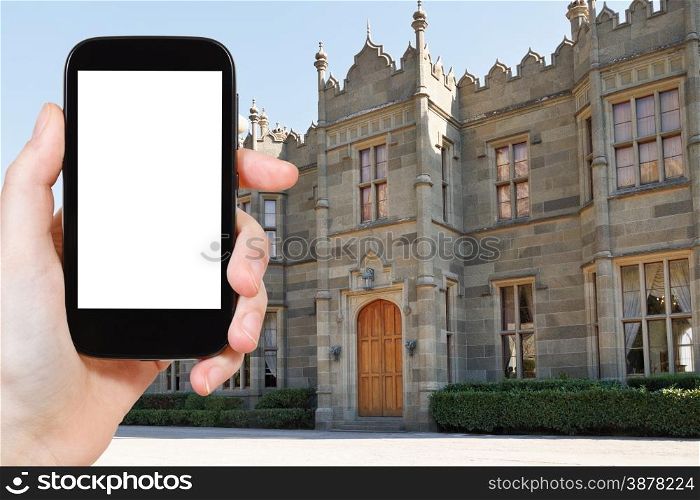 travel concept - tourist photograph northern entrance facade of Vorontsov (Alupka) Palace in Crimea on smartphone with cut out screen with blank place for advertising logo