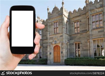 travel concept - tourist photograph northern entrance facade of Vorontsov (Alupka) Palace in Crimea on smartphone with cut out screen with blank place for advertising logo