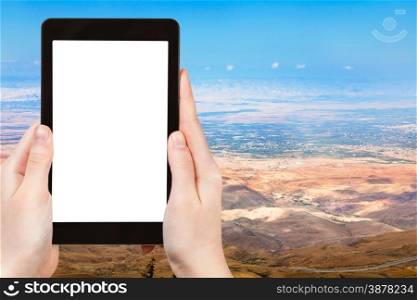 travel concept - tourist photograph Palestine Land from Mount Nebo in Jordan on tablet pc with cut out screen with blank place for advertising logo