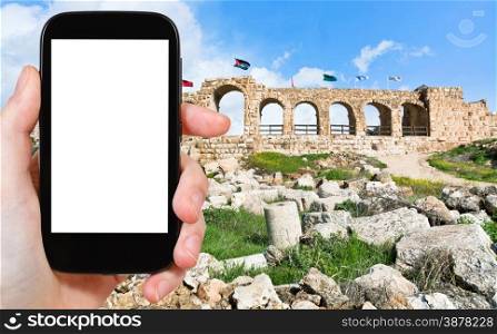 travel concept - tourist photograph the wall of Greco-Roman city of Gerasa (Jerash) in Jordan on smartphone with cut out screen with blank place for advertising logo