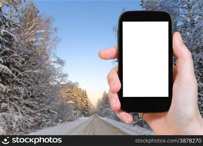 travel concept - tourist photograph winter road in snowy russian forest on smartphone with cut out screen with blank place for advertising logo