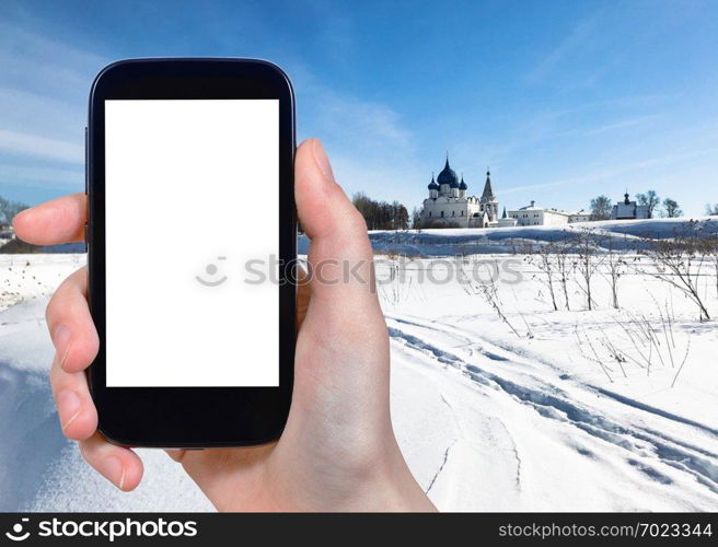 travel concept - tourist photographs of frozen river and Suzdal Kremlin with Chathedral and palace in Suzdal town in winter of Russia on smartphone with cutout screen with blank place for advertising