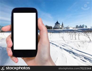 travel concept - tourist photographs of frozen river and Suzdal Kremlin with Chathedral and palace in Suzdal town in winter of Russia on smartphone with cutout screen with blank place for advertising
