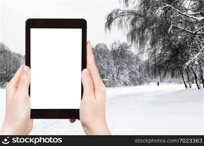 travel concept - tourist photographs of snow-covered city park in winter in Moscow city on smartphone with empty cutout screen with blank place for advertising