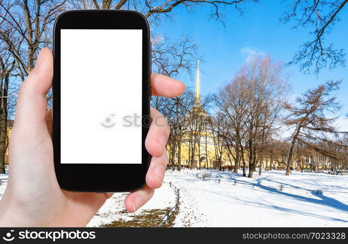 travel concept - tourist photographs of snow-covered path in Alexander Garden in Saint Petersburg city in March on smartphone with empty cutout screen with blank place for advertising