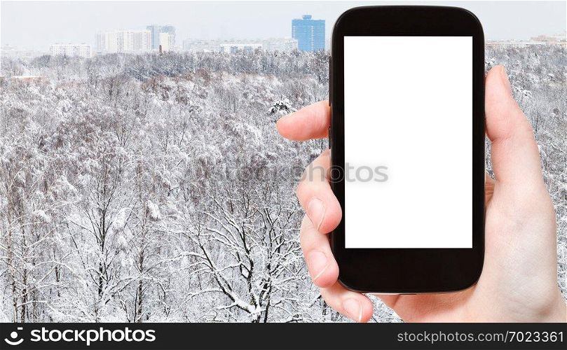 travel concept - tourist photographs of snowy city park and residential district in winter in Moscow city on smartphone with empty cutout screen with blank place for advertising