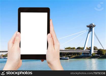 travel concept - tourist photographs of SNP Bridge (UFO bridge, Novy Most, New Bridge) over Danube river in Bratislava on tablet pc with cut out screen with blank place for advertising logo