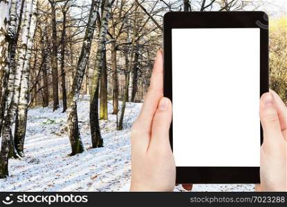 travel concept - tourist photographs of urban park covered with the first snow in sunny autumn day in Moscow Russia on smartphone with empty cutout screen with blank place for advertising