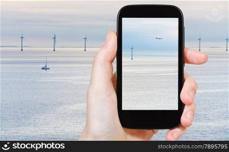travel concept - tourist shooting photo of Middelgrunden - offshore wind farm near Copenhagen, Denmark at early morning on mobile gadget