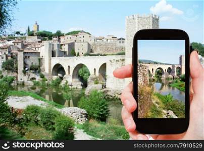 travel concept - tourist shoots photo of 12th-century Romanesque bridge over the Fluvia river in Besalu town on smartphone, Spain