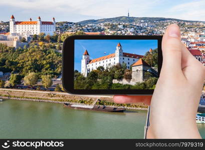 travel concept - tourist snapshot of Bratislava Hrad Castle over Danube River waterfront on smartphone