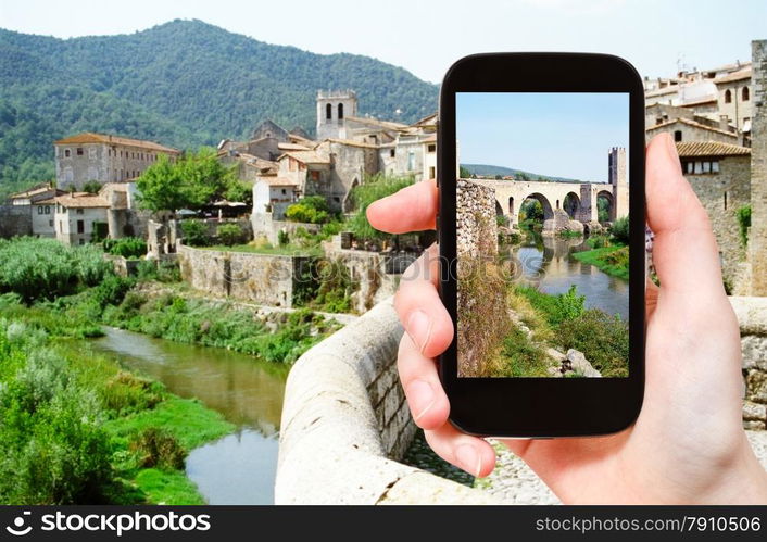 travel concept - tourist takes picture of 12th-century Romanesque bridge over the Fluvia river in Besalu town on smartphone, Spain