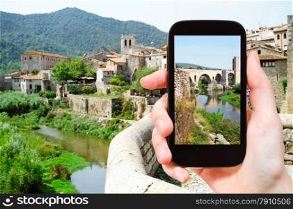 travel concept - tourist takes picture of 12th-century Romanesque bridge over the Fluvia river in Besalu town on smartphone, Spain