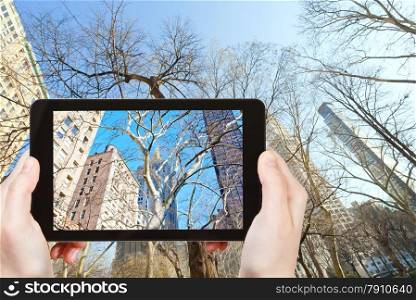travel concept - tourist takes picture of buildings and bare trees in New York in autumn on smartphone,