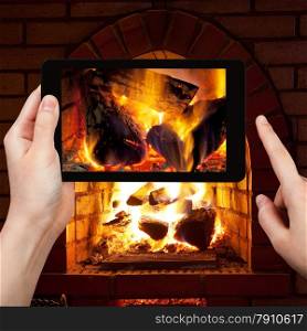 travel concept - tourist takes picture of burning wood in fireplace in evening time on smartphone,
