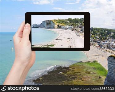 travel concept - tourist takes picture of Etretat resort village on english channel beach of cote d&rsquo;albatre, France on tablet pc