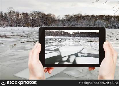 travel concept - tourist takes picture of floating of ice on river at early spring evening on smartphone, Moscow, Russia