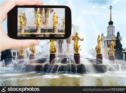 travel concept - tourist takes picture of Fountain Friendship of Nations at All-russia Exhibition Center in Moscow on smartphone,