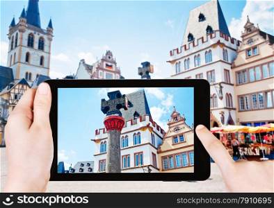 travel concept - tourist takes picture of medieval Market cross with medieval permission for town to have a market in Trier, Germany on smartphone,