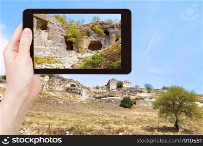 travel concept - tourist takes picture of medieval town chufut-kale on mountains of gorge mariam-dere in Crimea on smartphone