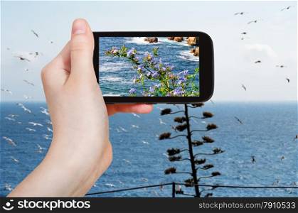 travel concept - tourist takes picture of mediterranean sea coastline in Costa Brava coast on smartphone, Spain