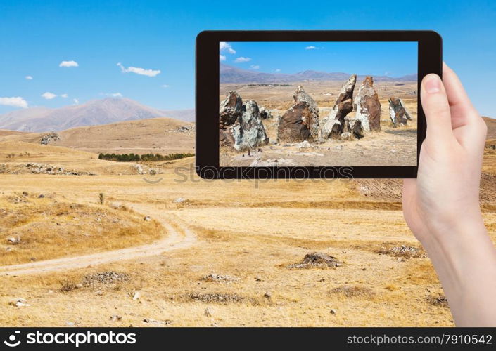 travel concept - tourist takes picture of megalithic standing stone of Zorats Karer (Carahunge) - pre-history monument in Armenia on smartphone,