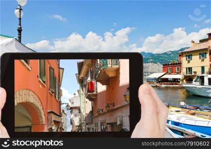 travel concept - tourist takes picture of narrow street to Lake Garda in Malcesine town, Italy on smartphone,