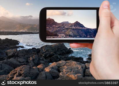 travel concept - tourist takes picture of sicilian town Taormina on sunset on smartphone