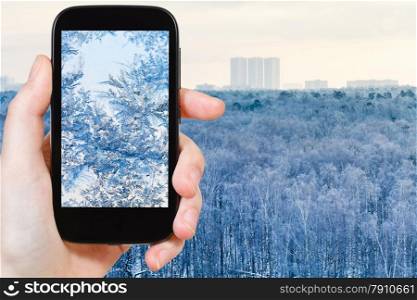 travel concept - tourist takes picture of snowflakes and frost on glass close up on smartphone,