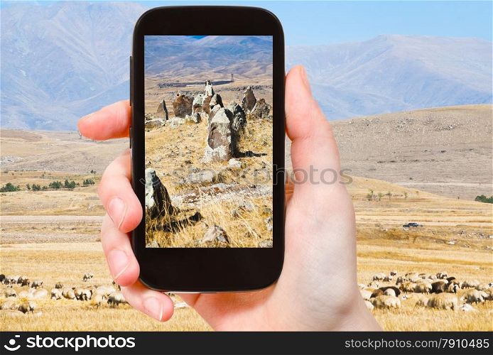 travel concept - tourist takes picture of standing menhirs of Zorats Karer (Carahunge) - pre-history megalithic monument in Armenia on smartphone,