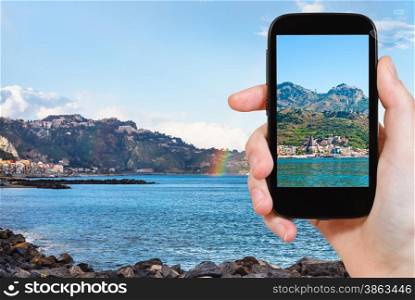 travel concept - tourist takes picture of town Taormina and Giardini Naxos beach, Sicily on smartphone