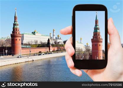 travel concept - tourist takes picture of Vodovzvodnaya Tower of Moscow Kremlin in spring day on smartphone,