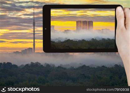travel concept - tourist takes picture of yellow sunrise and morning fog in autumn city on smartphone, Moscow