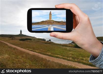 travel concept - tourist taking photo of ancient roman monument - lighthouse Tower of Hercules, La Coruna, Galicia, Spain on mobile gadget