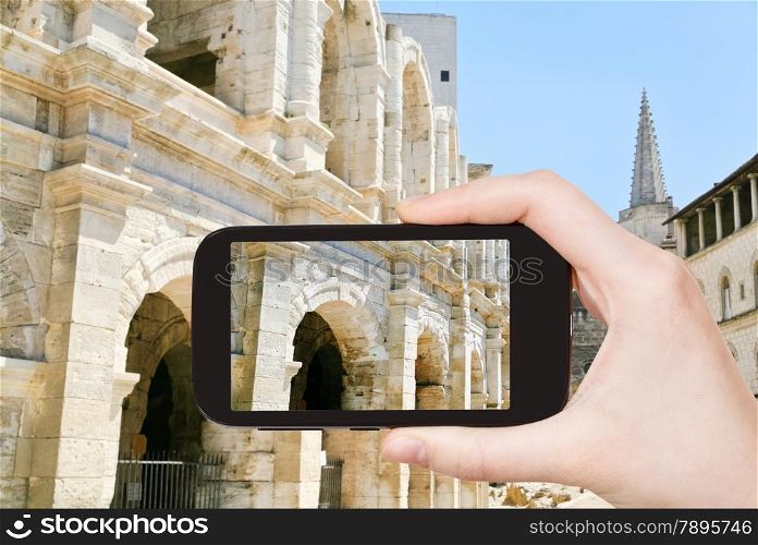 travel concept - tourist taking photo of Arles Amphitheatre Roman arena on mobile gadget, France