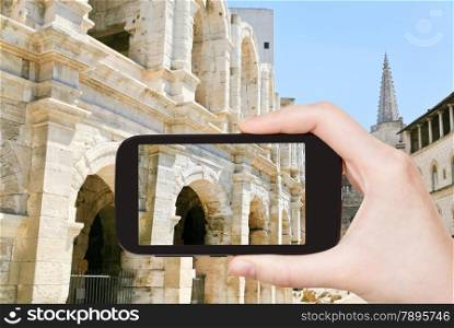 travel concept - tourist taking photo of Arles Amphitheatre Roman arena on mobile gadget, France