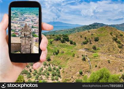 travel concept - tourist taking photo of calatabiano town on Etna slope on mobile gadget, Sicily, Italy