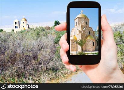 travel concept - tourist taking photo of church in Jordan river valley on mobile gadget