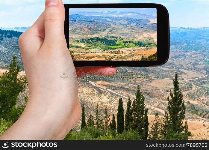 travel concept - tourist taking photo of Holy Land from Mount Nebo in Jordan on mobile gadget