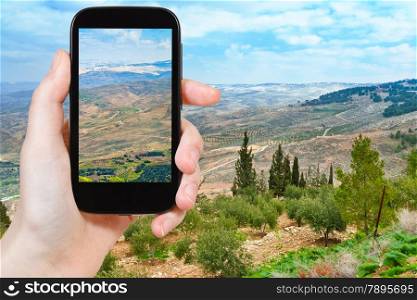 travel concept - tourist taking photo of Promised Land from Mount Nebo in Jordan on mobile gadget