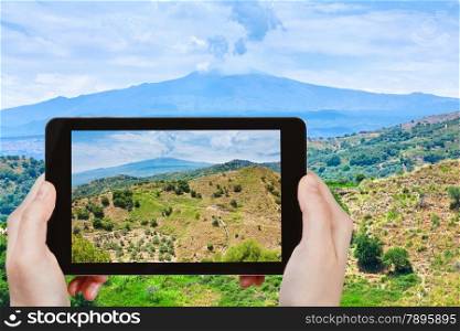 travel concept - tourist taking photo of rural landscape with Etna mount in Sicily on mobile gadget, Italy