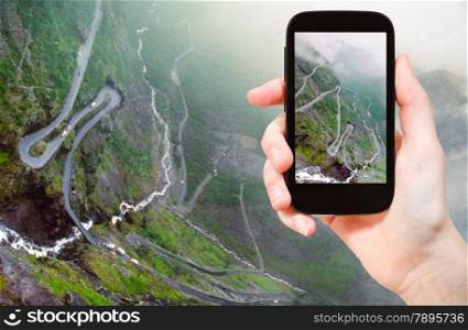 travel concept - tourist taking photo of Trollstigen (Trolls Path) serpentine mountain road in Norway on mobile gadget