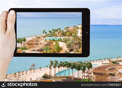 travel concept - tourist taking photo of waterfront on Dead Sea in Jordan on mobile gadget