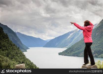 Travel concept. Tourist woman looking and pointing with finger at fjords beautiful mountains landscape in Norway. Woman tourist in norwegian mountains fjords