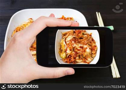 travel concept - visitor photographs of korean cuisine of kimchi appetizer  spicy nappa cabbage  in white bowl on smartphone