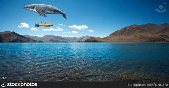 Travel concept. Whale floats in the air above the clouds carrying children in a yellow airplane.